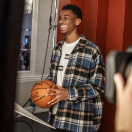 OGIO Clippers Shai Gilgeous-Alexander smiling during photoshoot against red holding basketball