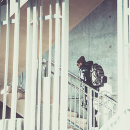 OGIO: Model with walking up white stairs with 525, MOD pack, 3-in-1 Jacket, and Badge Beanie and bars everywhere