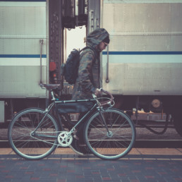 OGIO: Model with bike walking towards train with 525, MOD pack, 3-in-1 Jacket, and Badge Beanie from side